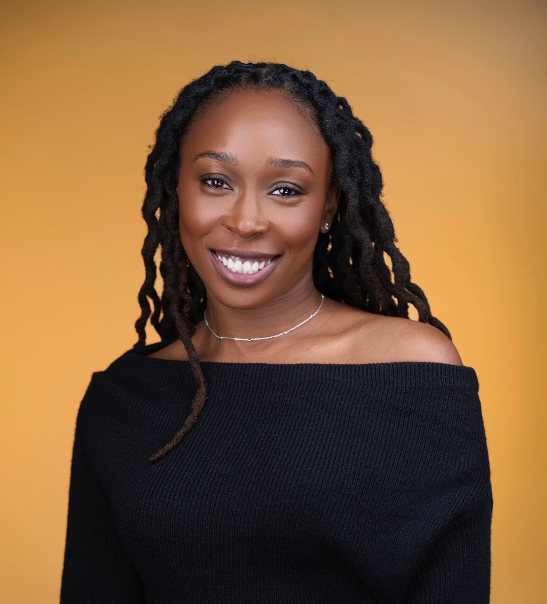 Dr. Bemi Fasalojo smiling, in a black off-shoulder sweater against a golden backdrop